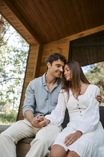 romantic man hugging cheerful woman while sitting on porch, holding hands, couple, vacation house - Fotó, kép