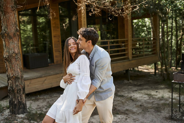 homem feliz abraçando mulher perto de casa de férias na floresta verde, verão e romance, casal apaixonado - Foto, Imagem