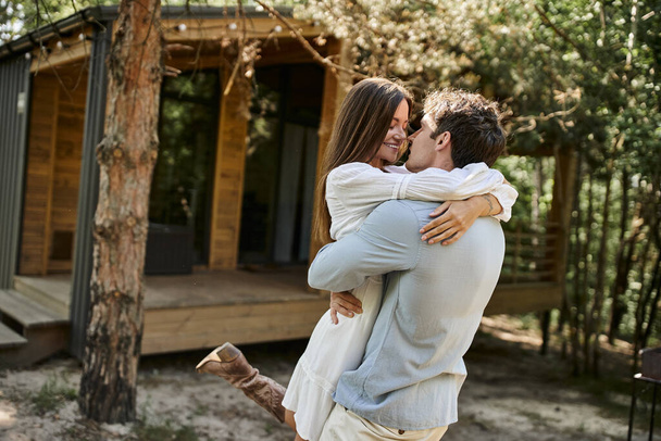 позитивний чоловік обіймає щасливу жінку в білому сараї, будинок відпочинку біля лісу, романтики і любові - Фото, зображення