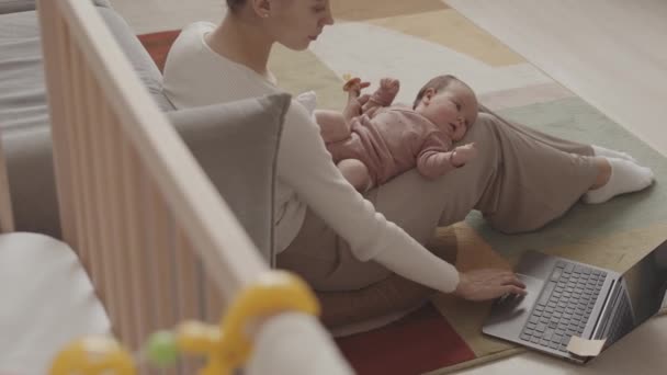 Slowmo of young Caucasian woman with infant daughter lying on her laps working on laptop from cozy home - Filmagem, Vídeo