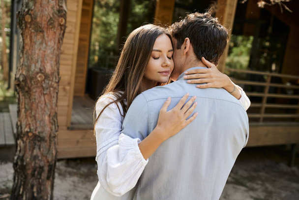 Brunette woman in sundress hugging boyfriend while standing near blurred vacation house outdoors - Zdjęcie, obraz