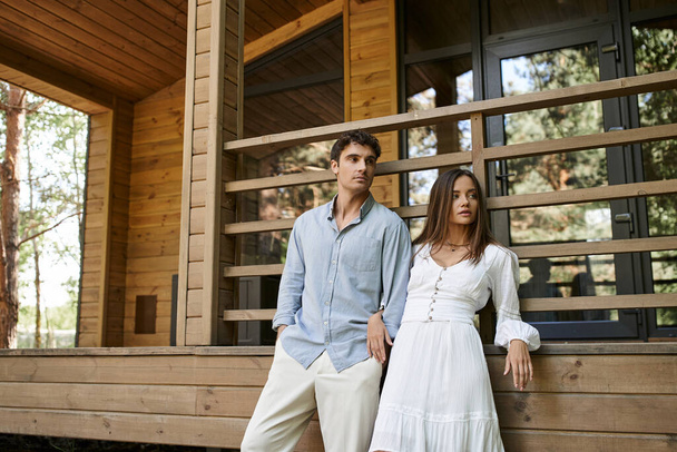 Trendy romantic couple in casual clothes looking away near vacation house outdoors at background - Foto, immagini