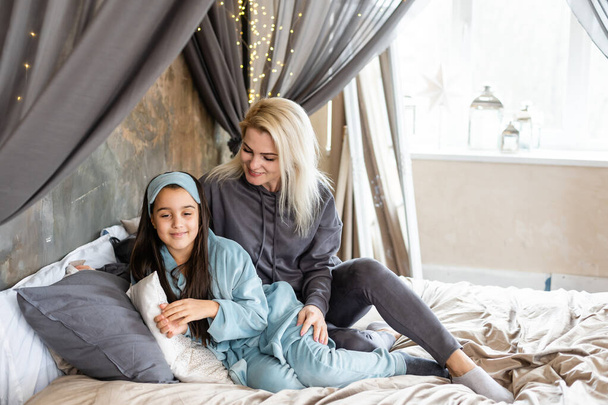 Мать и дочь лежат на кровати в пижаме и говорят о чем-то. Семейное время. - Фото, изображение
