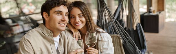 Hymyilevä brunette nainen halaamalla poikaystävä ja pitämällä viiniä terassilla loma talo, banneri - Valokuva, kuva