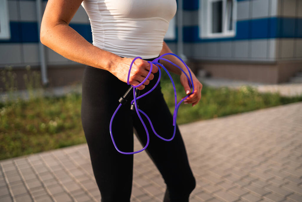Close-up woman in sportswear holding skipping rope outdoors, healthy active lifestyle. cardio workout equipment . High quality photo - Foto, immagini