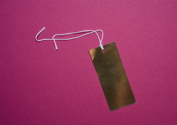 Golden price tag with a white string for clothing and merchandise on a pink background - Photo, Image