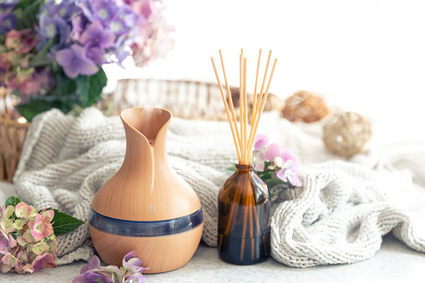 Spa composition with aroma oil diffuser lamp, flowers and knitted element on a blurred background, copy space. - Photo, Image