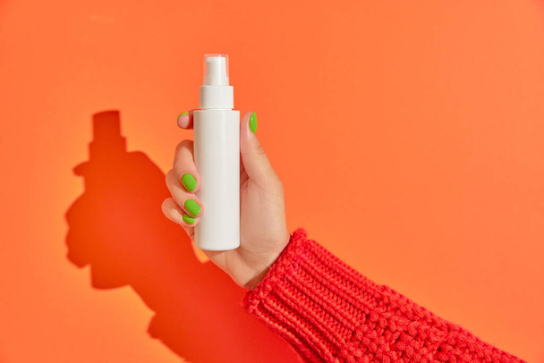 Womans hand holding cream container on orange background. Self care beauty treatment concept. Care products mockup template - Photo, Image
