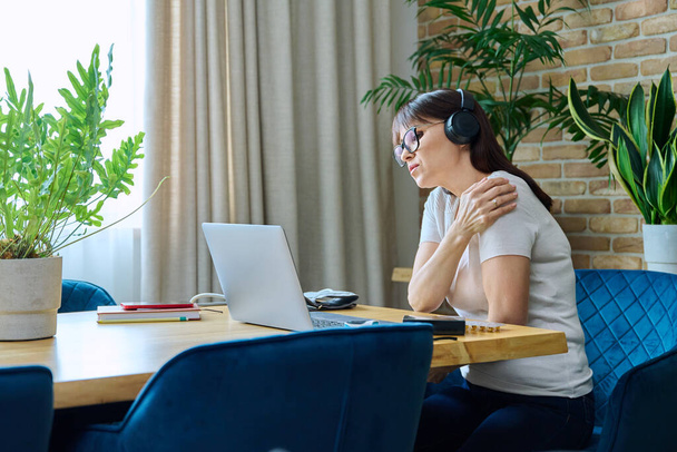 Middle aged woman in headphones having health problems, remote meeting video chat call with doctor on laptop, patient online consultation medical help. Health care, age, disease, telemedicine concept - Photo, Image