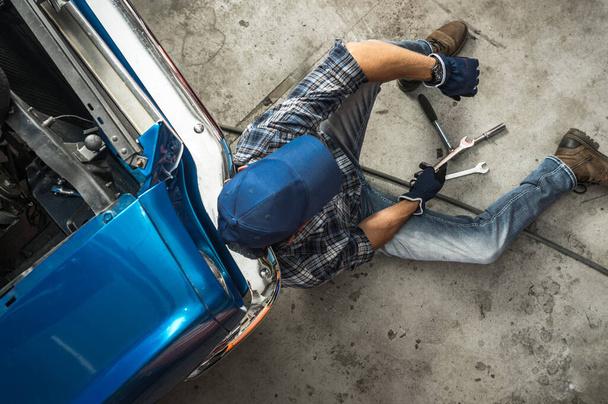 Fatigué Mécanicien de voitures classiques reposant sur un plancher de garage à côté de sa voiture musculaire cassée. Thème automobile. - Photo, image