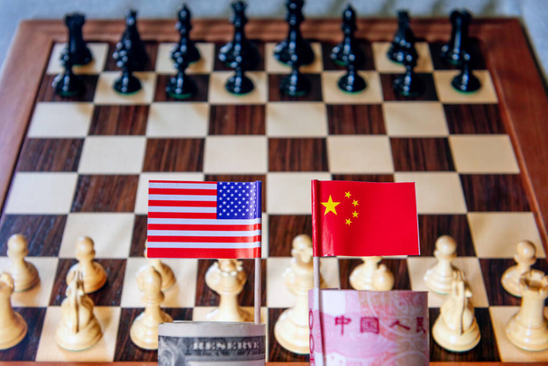 Ένα ρολό USD και κινεζικό Yuan με την εθνική σημαία κάθε χώρας με μια σκακιέρα στο παρασκήνιο. Μια έννοια του παγκόσμιου ανταγωνισμού και των συγκρούσεων στο χρηματοπιστωτικό εμπόριο. - Φωτογραφία, εικόνα