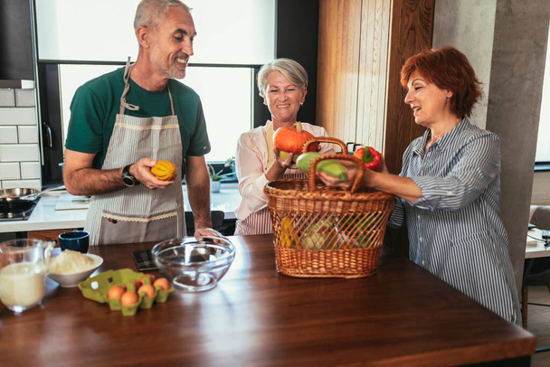 Щаслива зріла жінка середнього віку приносить свіжі овочі з країни своїм друзям, щоб зробити здорову вечерю - Фото, зображення