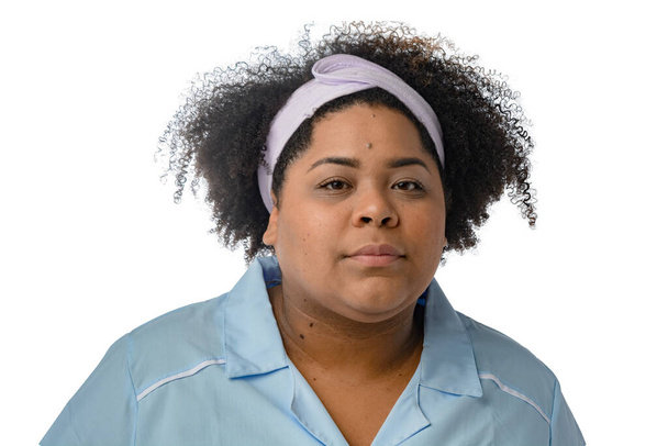portrait of brunette woman with a head band for facial cleansing wear blue uniform and looking at the camera seriously. white background - copy space. - Photo, Image