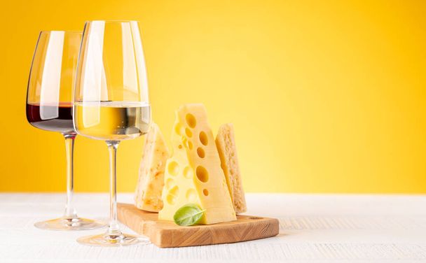 Güvertede çeşitli peynirler, kırmızı ve beyaz şarap. Kopyalama alanı olan sarı arkaplan - Fotoğraf, Görsel