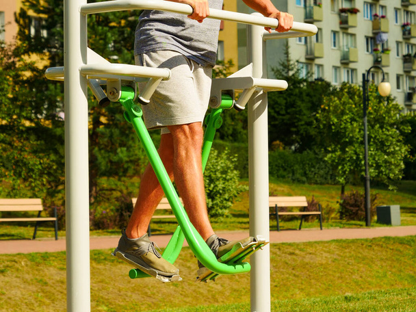 Young man working out in outdoor gym. Sporty guy doing legs exercises on street simulators. Staying fit and healthy. - Foto, immagini