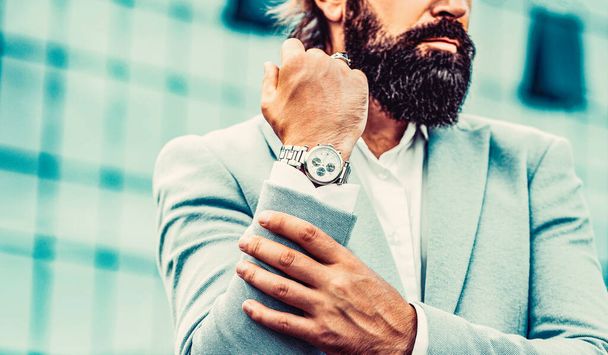 Mężczyzna trzyma zegarek. Portret odnoszącego sukcesy biznesmena w garniturze biznesowym, korzystającego z zegarka na tle miasta. - Zdjęcie, obraz