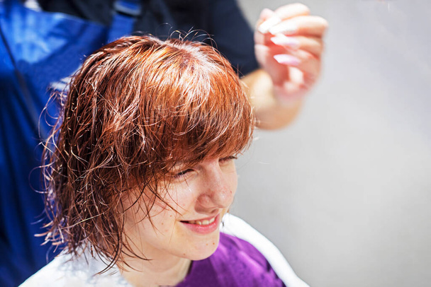 Руки парикмахера держат фен и сухую мокрую рыжую девушку после стрижки в салоне красоты - Фото, изображение
