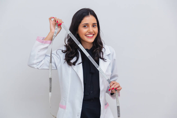 Brasiliano, donna caucasica indossa camice da laboratorio, tenendo il nastro di misurazione per la misurazione del corpo, dimagrante. - Foto, immagini