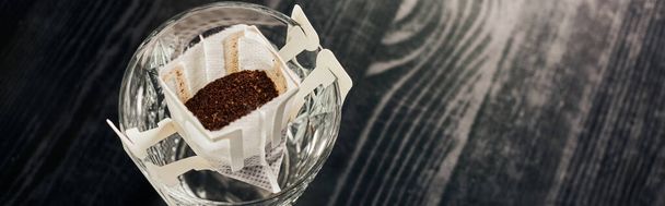 vetro con caffè macinato aromatico in sacchetto filtro su tavolo nero, metodo di produzione della birra, banner - Foto, immagini