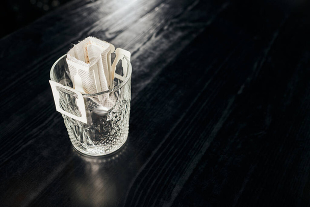 vetro con caffè macinato fresco e aromatico in sacchetto filtro su piano in legno nero, metodo pour-over - Foto, immagini