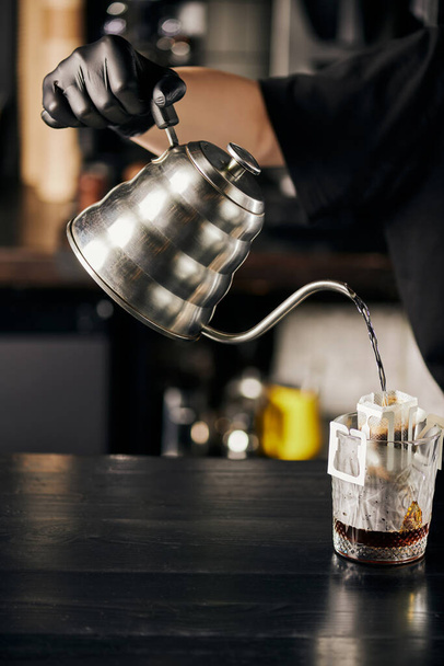 Kahveci espresso hazırlıyor, çaydanlıktan bardağa kaynar su döküyor filtre torbasında kahve var. - Fotoğraf, Görsel