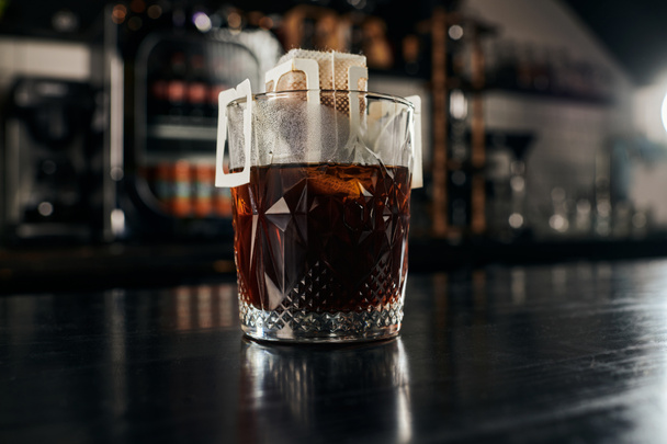 metoda kapání espressa, křišťálové sklo s kávou v papírovém sáčku na černém dřevěném stole v kavárně - Fotografie, Obrázek