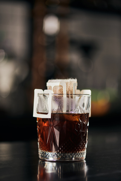 glas met gemalen koffie in papieren filterzak op zwarte toonbank, aromatische espresso, alternatieve methode - Foto, afbeelding