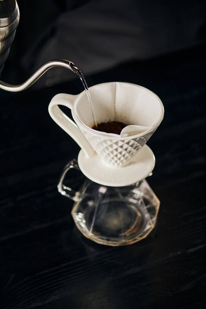 boiling water pouring on ground coffee in ceramic dripper placed on glass pot, V-60 style espresso - Photo, Image