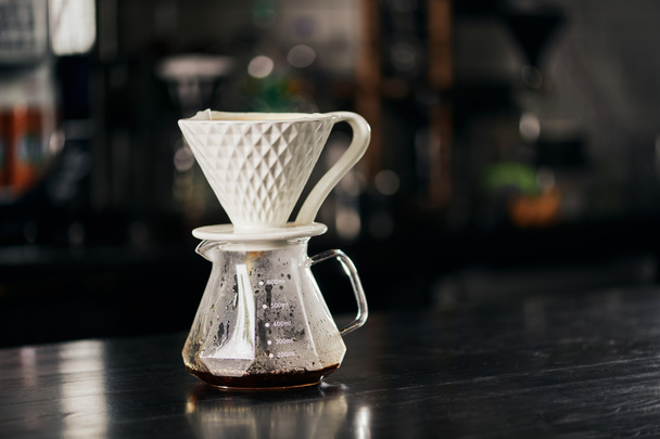 V-60 styl espresso metoda, keramické kapátko na skleněném hrnci s čerstvým přelévací kávou na černém stole - Fotografie, Obrázek