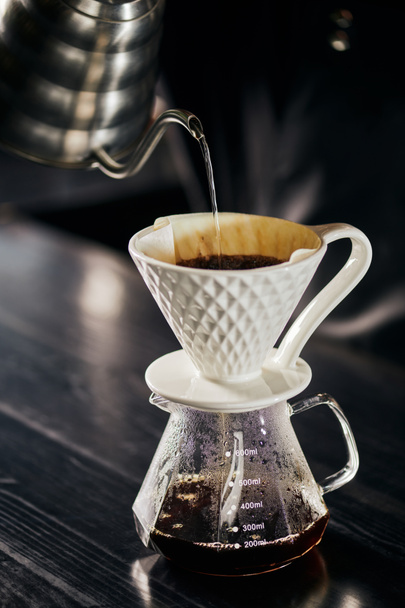 alternativa V-60 estilo espresso brew, agua hirviendo vertiendo en gotero de cerámica colocado en maceta de vidrio - Foto, Imagen