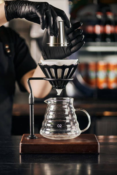 barista holding jigger above dripper stand with paper filter and glass coffee pot, V-60 style espresso - Photo, Image