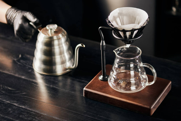 V-60 style brewing, barista with drip kettle near dripper stand with coffee filter above glass pot - Photo, Image
