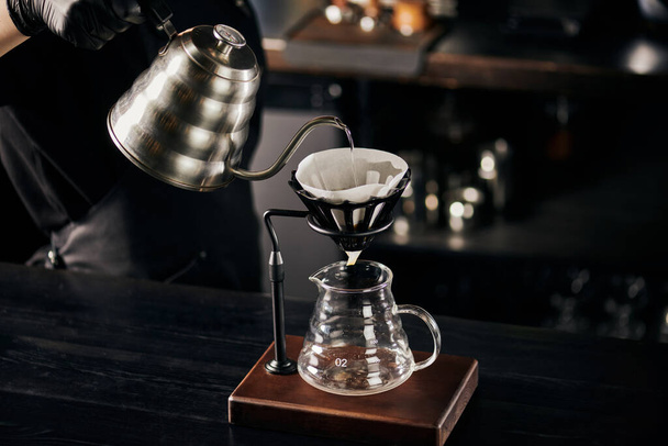 V-60 w stylu espresso, barista wylewa wrzącą wodę do filtra na stojaku nad szklanym garnkiem - Zdjęcie, obraz