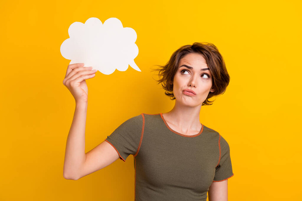 Portrait of minded confused woman wear khaki top look at mind cloud in hand empty space plump lips isolated on yellow color background. - Foto, afbeelding