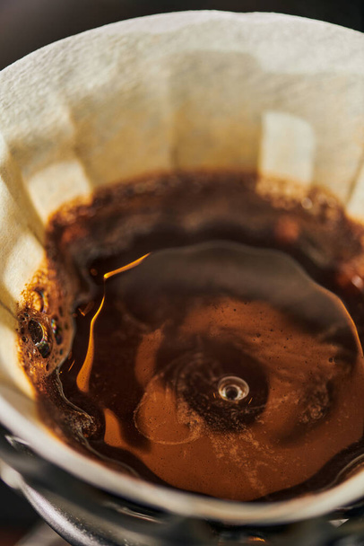 vue rapprochée du café expresso noir de style V-60 fraîchement brassé avec mousse dans un sac filtrant en papier - Photo, image