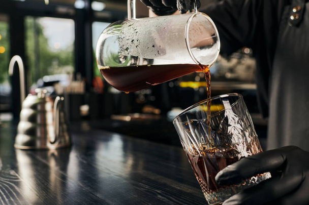 μερική άποψη του barista ρίχνει αρωματικό espresso από την καφετιέρα σε κρύσταλλο γυαλί στην καφετέρια - Φωτογραφία, εικόνα