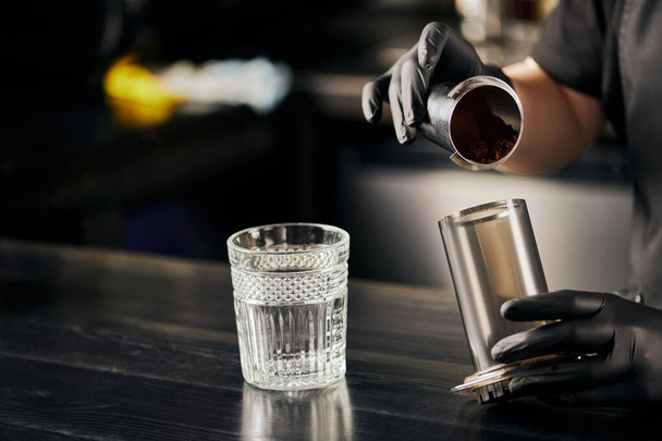 vista parcial de barista em vidro de látex preto segurando aero imprensa com café perto de vidro na mesa preta - Foto, Imagem