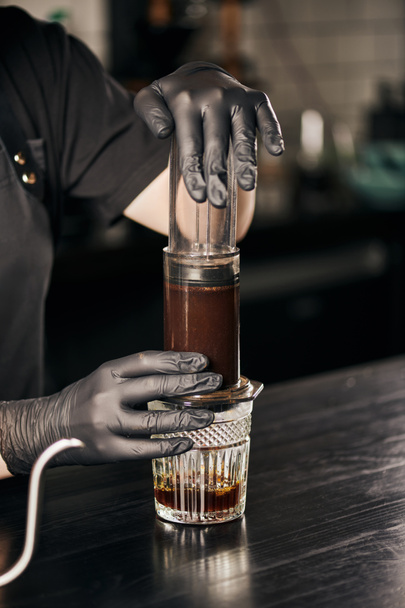 cropped view of barista in black gloves pressing ground coffee in aero press while preparing espresso - Photo, Image