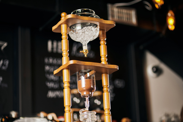 alternatieve espresso brouwsel, lage hoek uitzicht op koud druppelkoffiezetapparaat met ijsblokjes en gemalen koffie - Foto, afbeelding