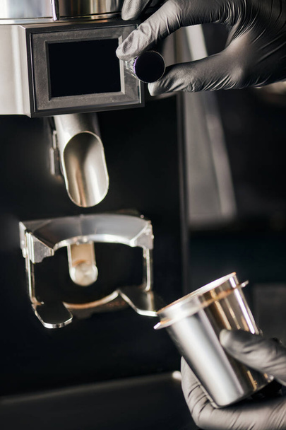 vista cortada de barista em luvas pretas com copo de medição perto moedor de café elétrico, equipamentos - Foto, Imagem