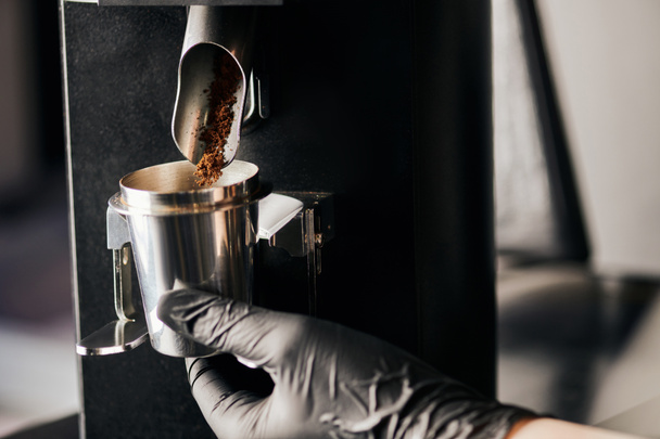 barista in black latex glove holding measuring cup near ground coffee and electric coffee grinder - Photo, Image