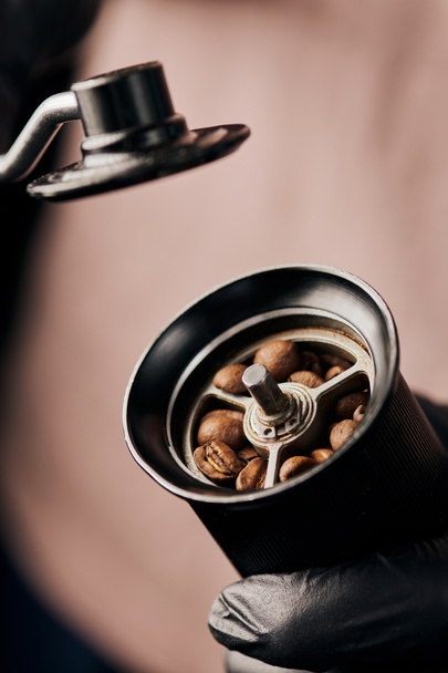 καλλιεργημένη άποψη του barista κρατώντας χειροκίνητο μύλο καφέ με κόκκους καφέ, Arabica, κοντινό πλάνο, ενέργεια  - Φωτογραφία, εικόνα