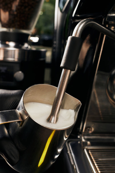 zugeschnittene Ansicht von Barista Milchaufschäumer in Krug, schäumende Milch, professionelle Kaffeemaschine, Latte  - Foto, Bild