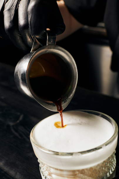 Barista in Latexhandschuhen bereitet Latte Macchiato zu, gießt Espresso, Kanne mit Kaffee, Makro - Foto, Bild