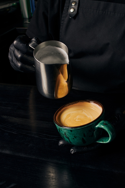 barista het bereiden van cappuccino, met kruik met melk, kopje met espresso, arabica, energie  - Foto, afbeelding