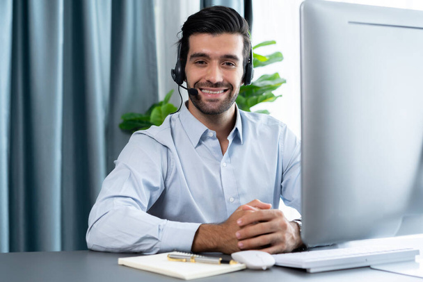 Male call center operator or telesales representative siting at his office desk wearing headset portrait. Customer service agent with smiling to camera on workplace. fervent - Фото, зображення