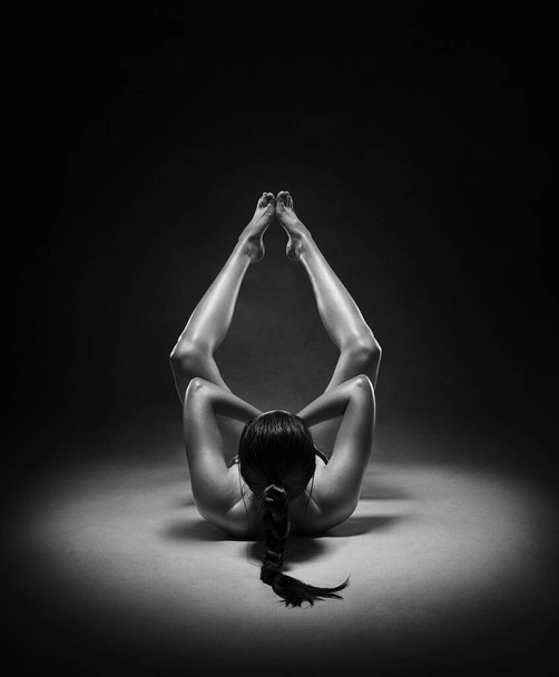 Beautiful nude sexy fitness girl with great figure flexing her perfect body in a yoga pose at the studio. Black and white photo - Фото, зображення