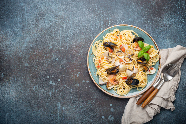Włoski makaron z owoców morza spaghetti z małżami, krewetki, małże w sosie pomidorowym z zielonej bazylii na talerzu na rustykalnym niebieskim tle betonu nad głową. Kuchnia śródziemnomorska, miejsce na tekst - Zdjęcie, obraz
