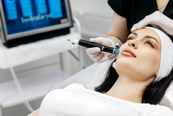 Pleasant relaxation. Beautiful young woman closing her eyes while having a hydrafacial procedure - Photo, Image