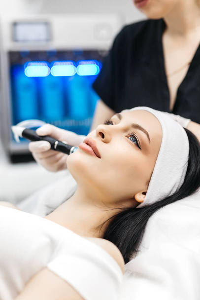 Pleasant relaxation. Beautiful young woman closing her eyes while having a hydrafacial procedure - Foto, afbeelding